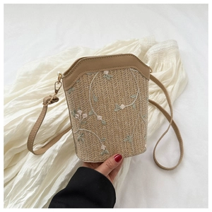 Detailed close-up of straw bucket bag featuring colorful floral embroidery and leather strap