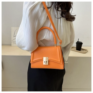 Detail of a bright orange crossbody bag featuring a metal lock and woven handle for women