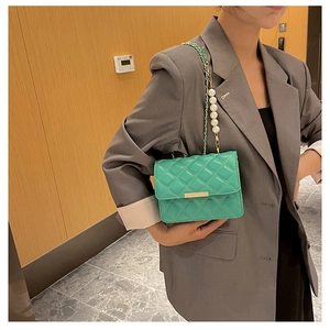Détail du sac à bandoulière matelassé vert avec chaîne en perles sur un costume gris