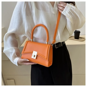 Detailed view of bright orange crossbody bag featuring woven handle and metal twist lock
