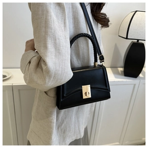 Detail of black crossbody bag featuring a woven handle and gold metal square lock