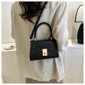 Detail of black trapezoid bag with woven handle and gold lock on beige textured blazer