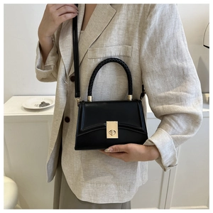 Close-up of black leather handbag featuring a woven handle and gold twist lock clasp