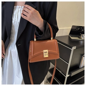 Detail of a brown leather-style handbag featuring a gold lock and woven top handle