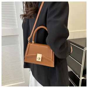 Close-up of brown leather handbag with woven handle and gold clasp on a model