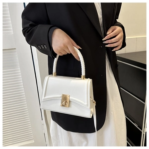 Close-up of white structured handbag featuring a woven top handle and gold twist lock clasp