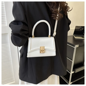 Close-up of a white leather crossbody bag with a braided handle and gold twist lock