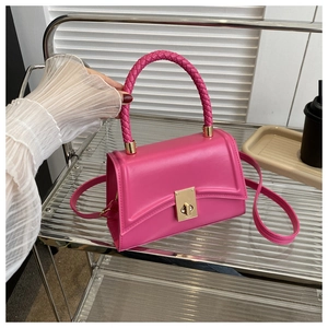 Detail of rose pink handbag featuring woven handle, gold lock, and curved base design