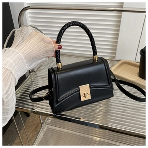 Detail of black crossbody bag featuring a gold twist lock and woven leather handle