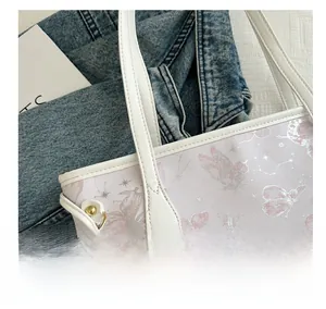 Close-up of butterfly print on white tote bag with leather texture and gold hardware details