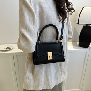 Elegant black leather square handbag with woven handle and gold lock worn by a model