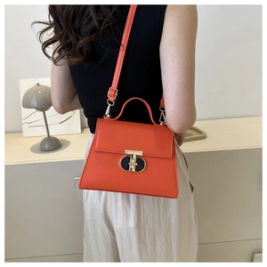 Detail of a bright orange crossbody bag featuring a unique gold and black metal lock