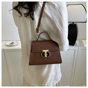 Dettaglio di una borsa a trapezio in pelle marrone con fibbia a T dorata e manico superiore