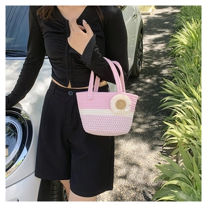 Detail of pink and white striped woven bucket bag with flower charm in outdoor setting