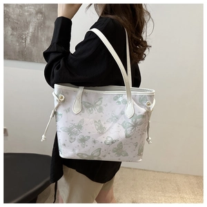 Detail of white tote bag with green butterfly print showing the shoulder strap on a model