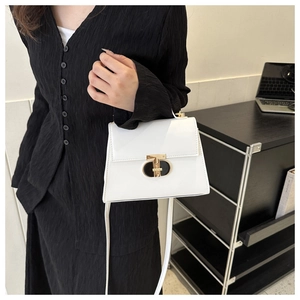 Detail of white PU leather crossbody bag featuring a modern gold T-shaped metal clasp