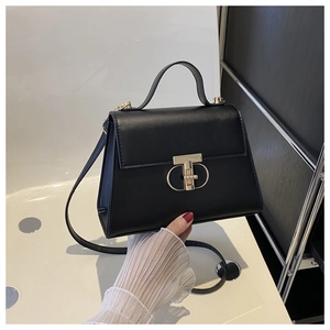 Detail of black leather handbag featuring a prominent gold T-shaped rotating metal clasp