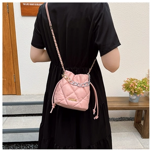 Detail of pink quilted bucket bag with chain strap and metal logo on black dress