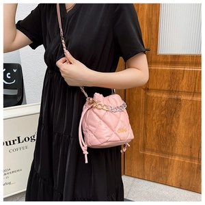 Detail of pink quilted bucket bag featuring a gold metal logo and chain shoulder strap