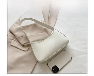 Flat lay of a minimalist white leather hobo bag on a blazer with stylish accessories