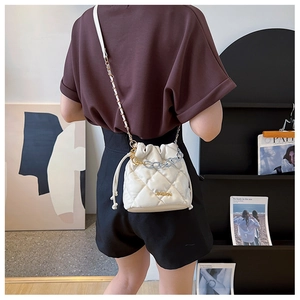 Quilted white bucket bag with chain strap shown on a model in a minimalist setting