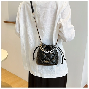 Detailed view of black quilted bucket bag featuring a metal logo and mixed chain strap