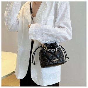 Detailed view of black quilted bucket bag featuring a gold chain strap and drawstring closure