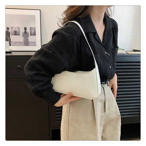 Detail view of cream white minimalist underarm bag worn over the shoulder by a model