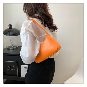 Close-up of bright orange minimalist hobo shoulder bag styled with white shirt