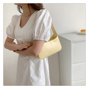 Close-up of a minimalist pale yellow underarm bag with smooth leather texture on a model