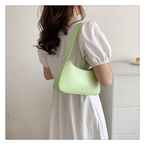 Model wearing a light green matte leather underarm baguette bag against white background