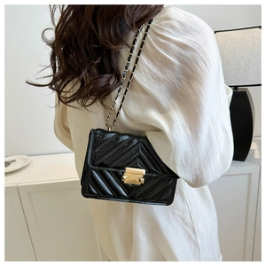 Close-up of black patent leather crossbody bag with V-quilted stitching and gold lock