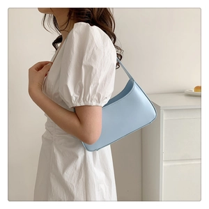 Model wearing a light blue minimalist baguette bag with a white dress in a home setting