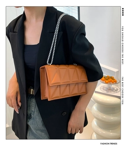 Detail of orange quilted crossbody bag featuring a silver chain strap and metal lock