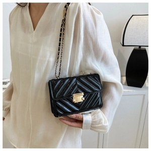 Detail of black patent leather crossbody bag with chevron quilting and gold clasp