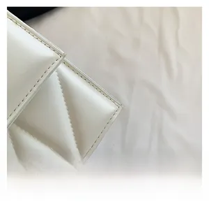 Detail shot of white quilted faux leather texture with precise stitching on small square bag