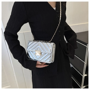 Close-up of silver crossbody bag with chevron quilting and golden metal chain strap