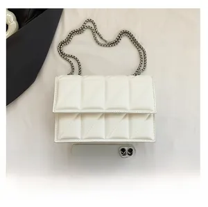 White quilted crossbody bag with silver chain strap shown next to a smartphone for scale