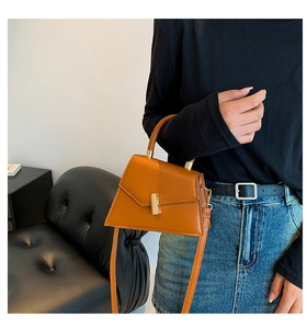 Close-up of brown leather bag with golden geometric clasp and cylindrical handle detail