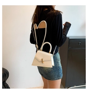 Detailed side view of white trapezoid handbag with gold rotating lock on female model