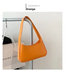 Detail view of the orange minimalist hobo shoulder bag hanging on a metal stand