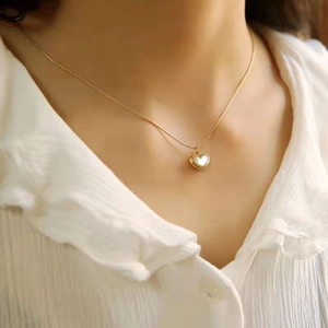 Élégant collier coeur doré avec nacre blanche porté sur le cou d'une femme chic