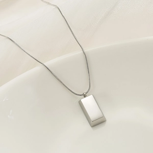 Macro shot of a minimalist silver rectangular pendant necklace on a satin silk background