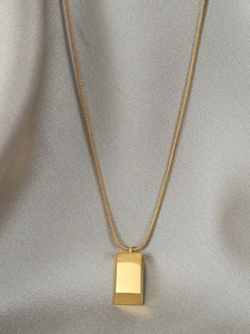 Detailed shot of a gold brick pendant on a sleek snake chain over grey silk fabric