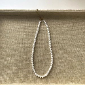 Collier de perles élégant de 7mm avec fermoir doré sur un plateau beige texturé