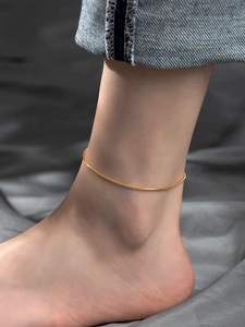 Close-up of a minimalist golden snake bone anklet on an ankle with a dark background