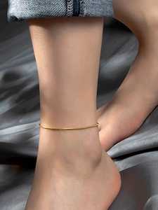 Close-up of minimalist gold snake bone anklet on model with silk fabric background