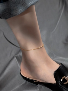 Close-up of a sleek gold snake chain anklet worn by a model with black mules