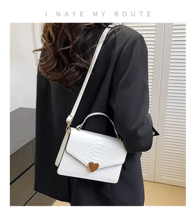 Detailed view of white crocodile pattern square bag with gold heart clasp on a model