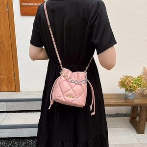 Pink quilted bucket bag with gold logo and dual chain straps shown in a stylish scene